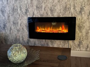 Ein Kamin mit modernem Design, eine dekorative Glasobjekt auf einem Holztisch und eine strukturierte Wand im Hintergrund.