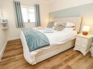 A bedroom with a bed, bedside table, lamp, and a window with curtains. - The Old Post Office (Ventnor)