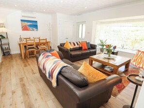 A living room with a sofa, a coffee table, and a dining area with chairs and a table. - The Old Post Office (Ventnor)