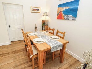 A dining area with a wooden table set for six, a white door, a framed picture, and a lamp. - The Old Post Office (Ventnor)