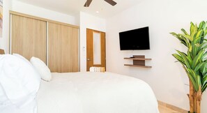 A hotel room with a bed, a TV, a wooden wardrobe, and a potted plant. - 1BR condo w/ pool & gym (Playa del Carmen)