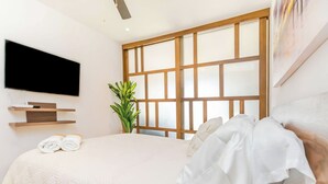 Quarto moderno com cama grande, televisão de tela plana na parede, planta em vaso e um quadro.