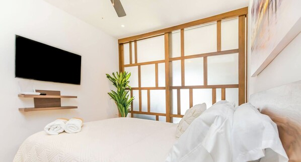 Camera da letto moderna con un letto grande, una TV a schermo piatto montata a parete, una pianta in vaso e un quadro.