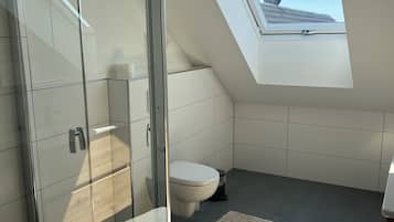 Ein modernes Badezimmer mit Oberlicht, einer Duschkabine aus Glas und einer Toilette.