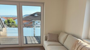 A modern living room with a sofa, a patterned rug, and a view through a glass door to a balcony.
