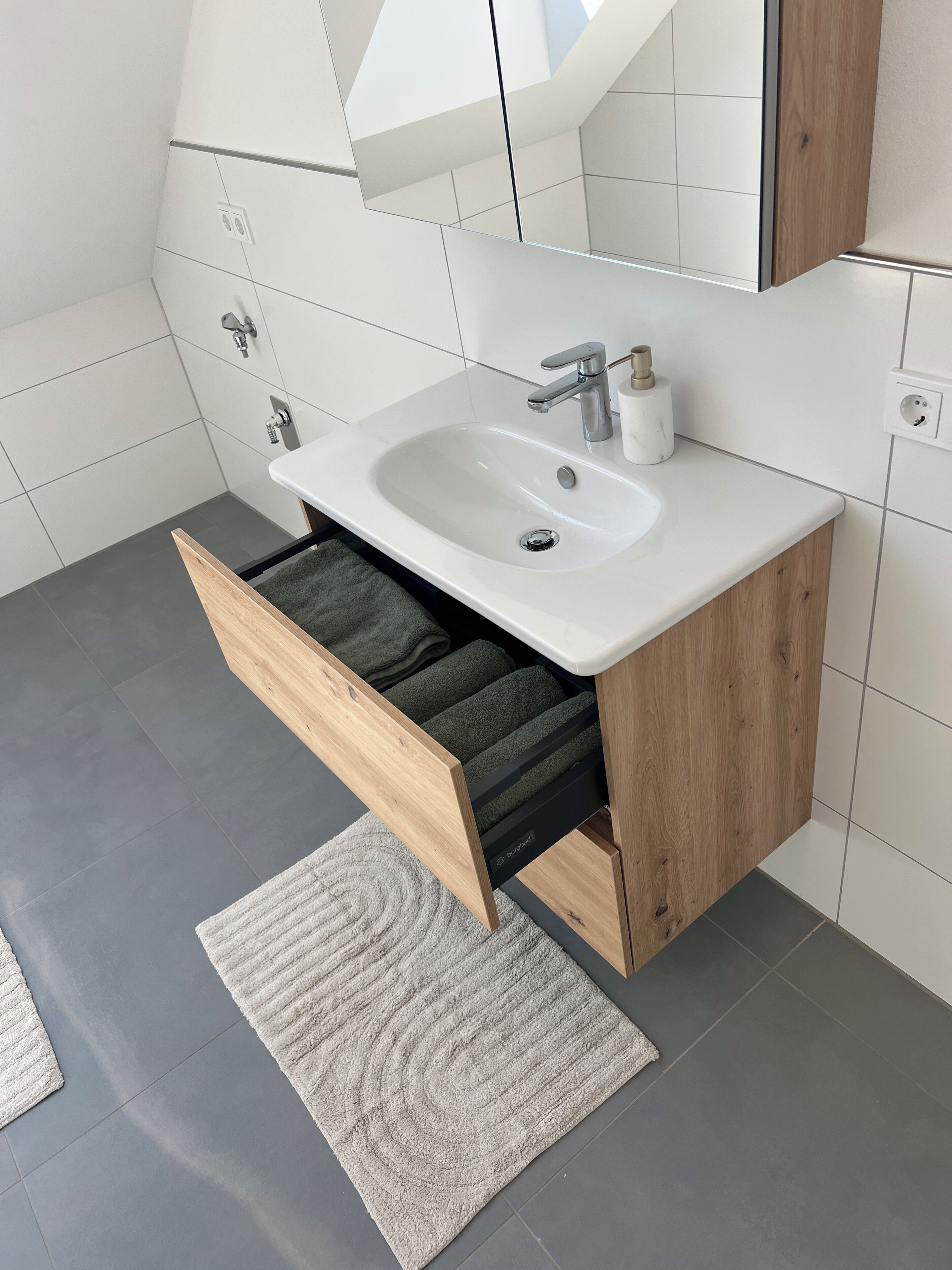 A modern bathroom with a white sink, wooden cabinet, and a towel rack.