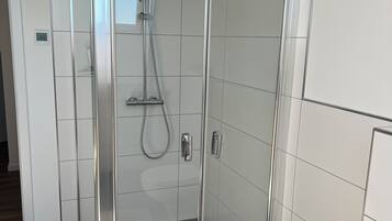 Ein modernes Badezimmer mit einer gläsernen Duschkabine, weißen Fliesen und einer sichtbaren Toilette.