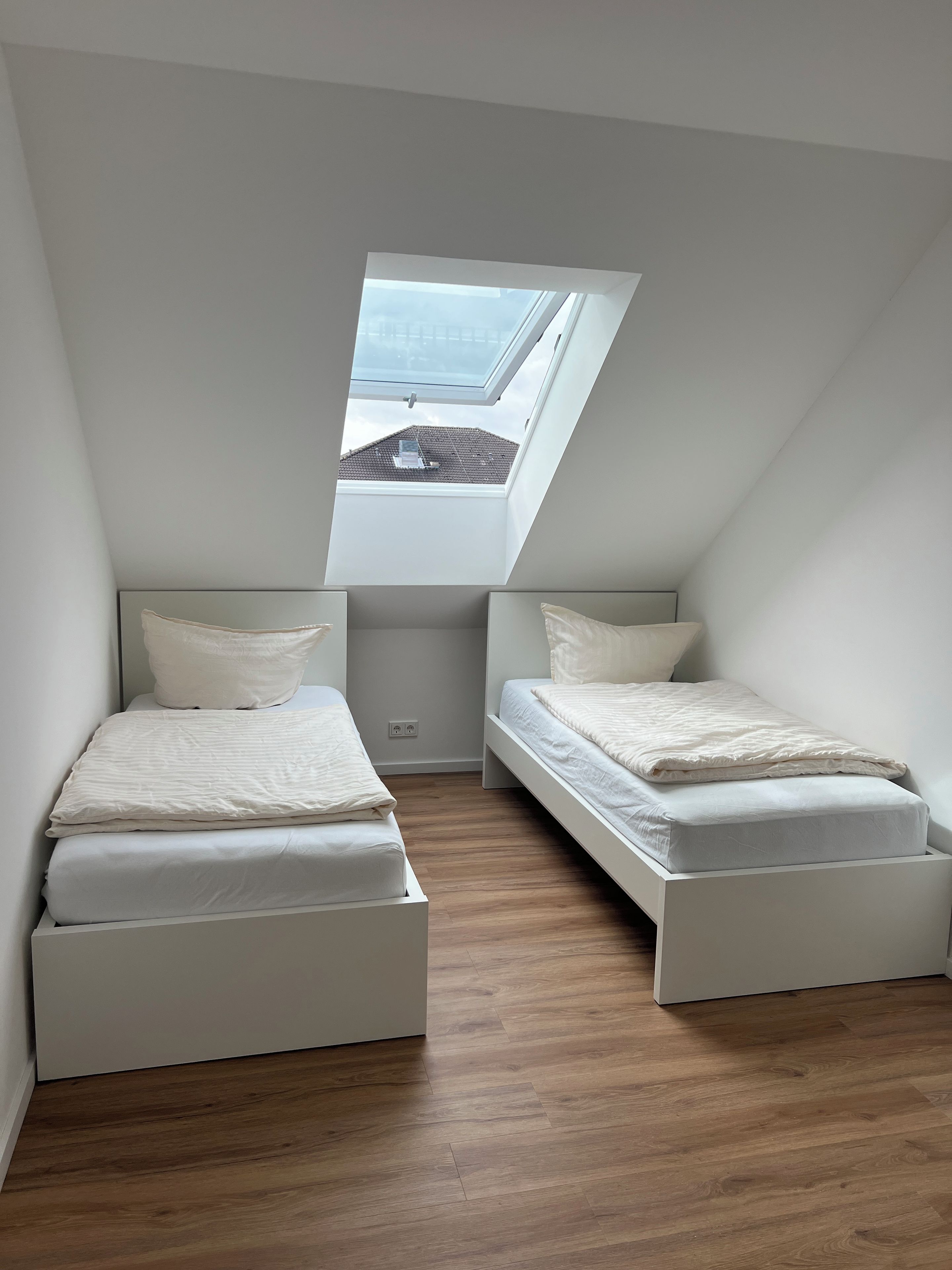 Ein kleines, modernes Schlafzimmer mit zwei Betten, einem Oberlicht und Holzboden.