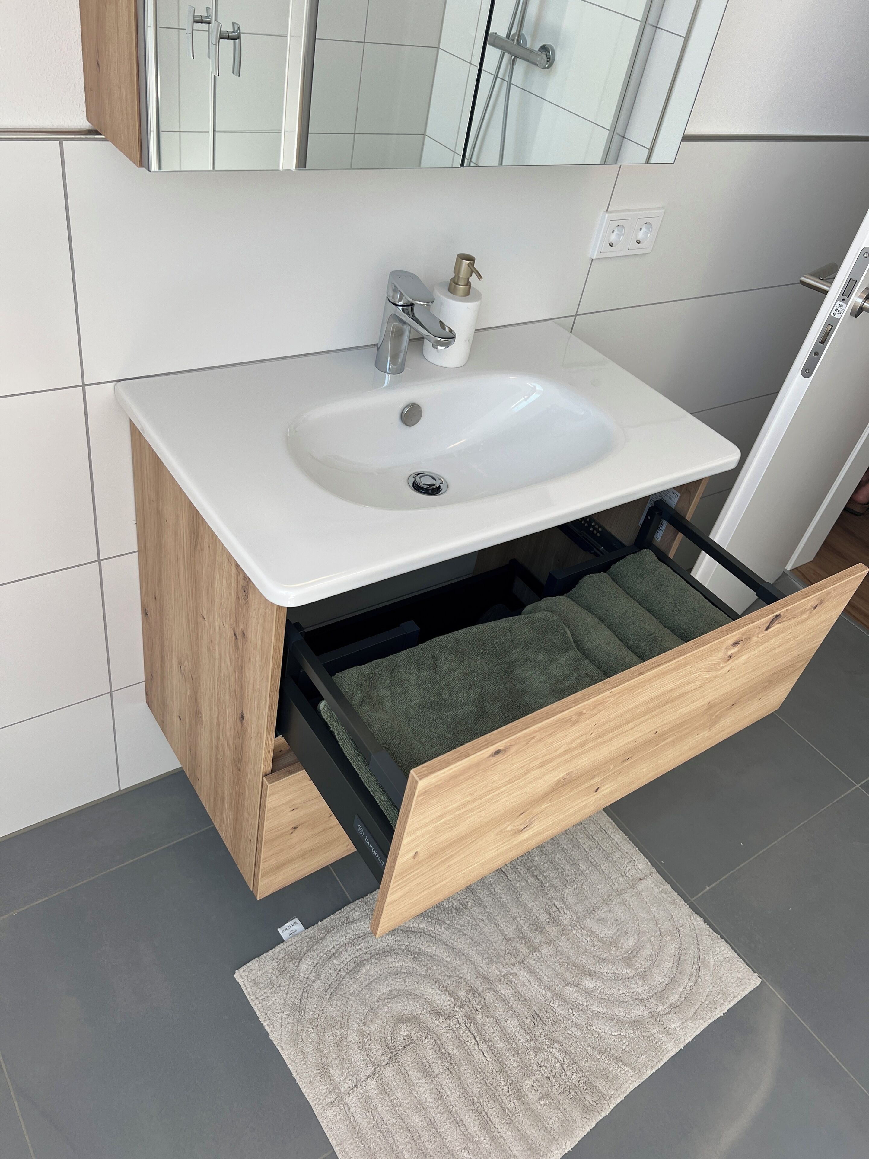 Un baño con un lavamanos blanco, un perchero, un espejo y un armario de madera.