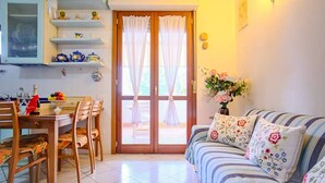 Ein Essbereich mit Tisch und Stühlen, eine Küche mit Regalen sowie ein Wohnzimmer mit Sofa und Zierkissen.