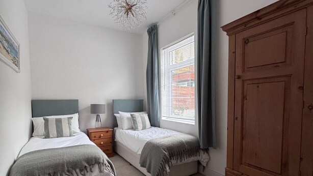 Een slaapkamer met twee bedden, een kledingkast, een nachtkastje en een raam met gordijnen.