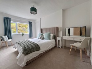 Un dormitorio con cama, escritorio, silla, ventana con cortinas e iluminación en el techo.