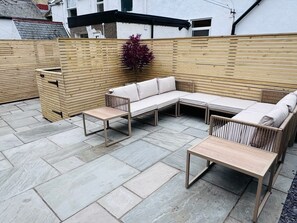 Un patio con un banco de madera, una mesa y un espacio de descanso con cojines.
