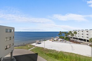 Blick auf einen Strand mit einem Gebäude, Palmen und wolkenlosem Himmel.