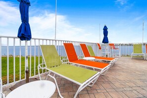Une terrasse avec des chaises et des tables en métal blanc, une clôture blanche et une vue sur la mer.