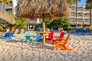Une zone de plage avec des fauteuils Adirondack aux couleurs vives et un parasol en chaume.