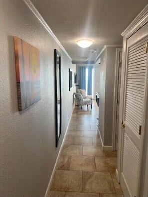 Un couloir avec un sol carrelé, un tableau accroché au mur et une porte sur la droite.