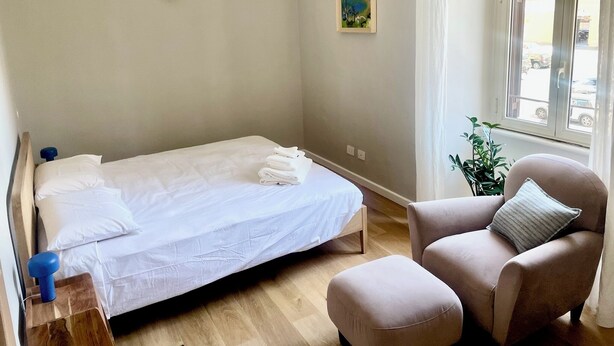 A minimalist room with a bed, a chair, a small table, a window with a view, and a painting on the wall. - Rooms with a View, Trastevere Home Rental (Roma)