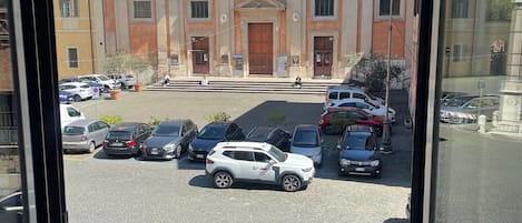 A building with a central dome and a cross on top, surrounded by parked cars and a cobblestone street.