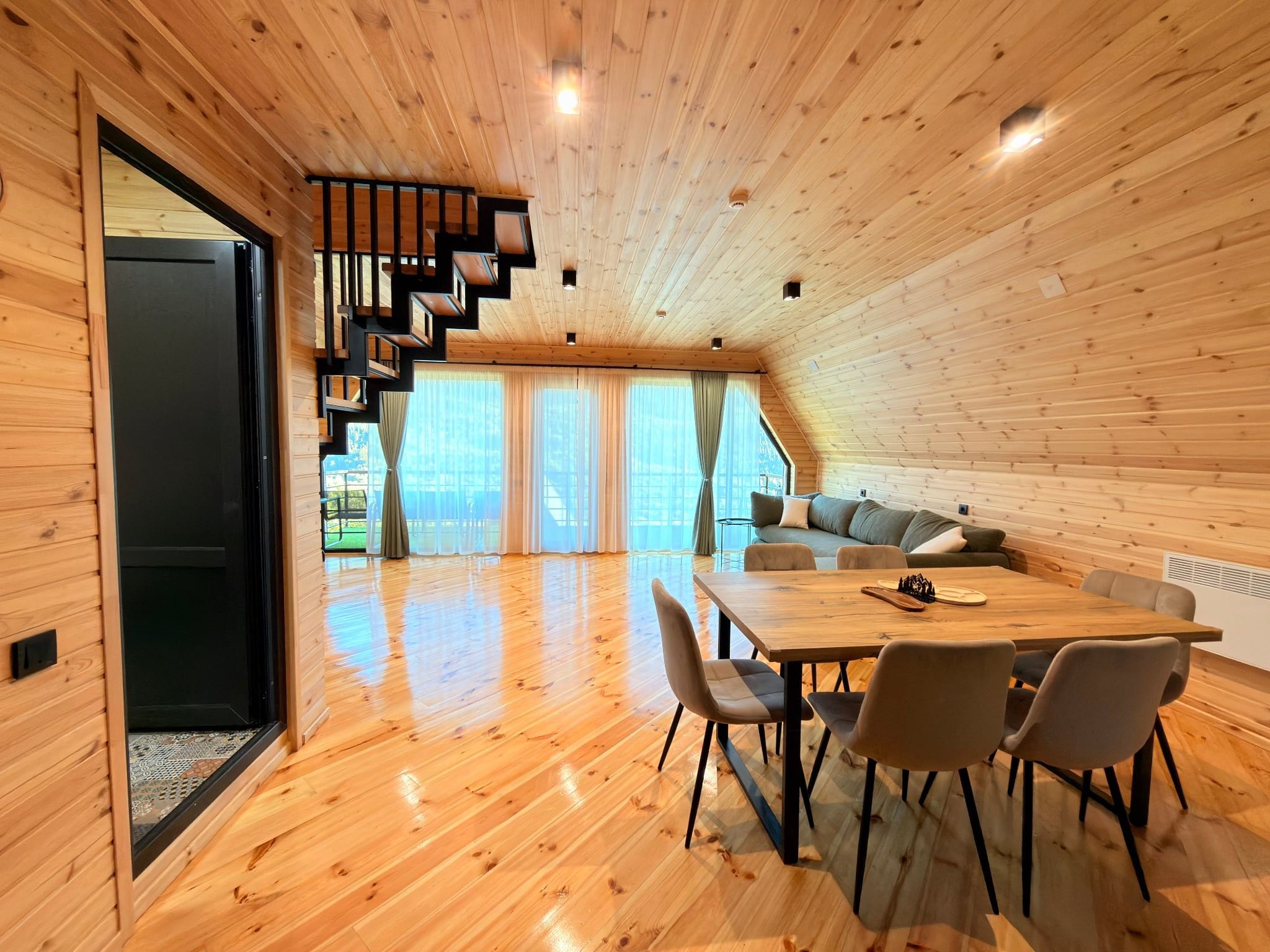 Un interior de madera con zona de comedor, sofá y escalera.