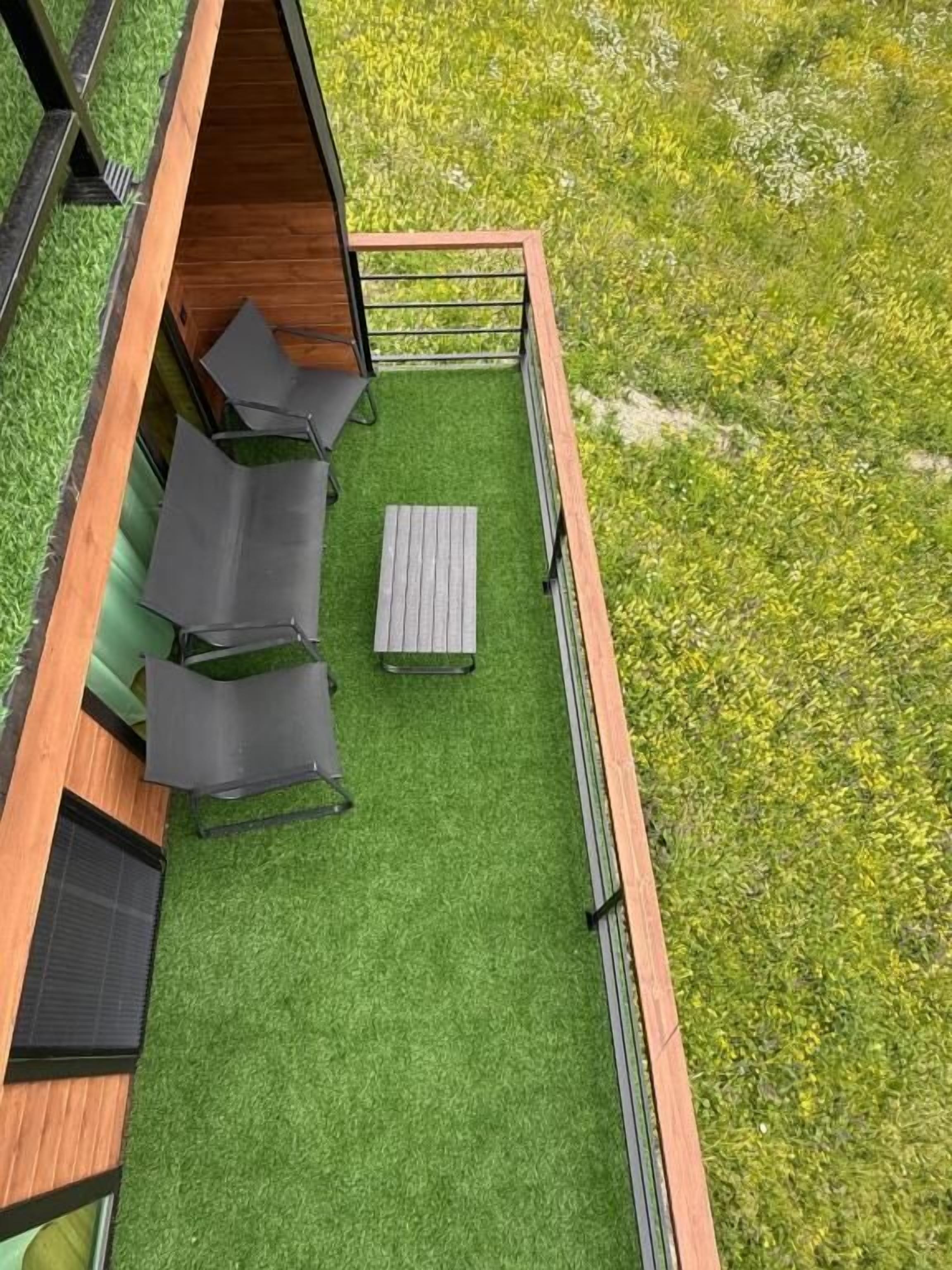 A rooftop terrace with artificial grass, a wooden deck, and a seating area with chairs and a table.