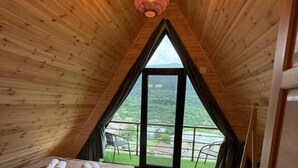 Un interior de madera con una cama, una lámpara colgante y un ventanal grande.