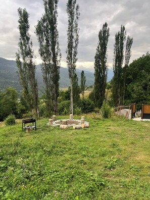 A grassy outdoor area with a circular arrangement of logs, a bench, and a wooden structure.