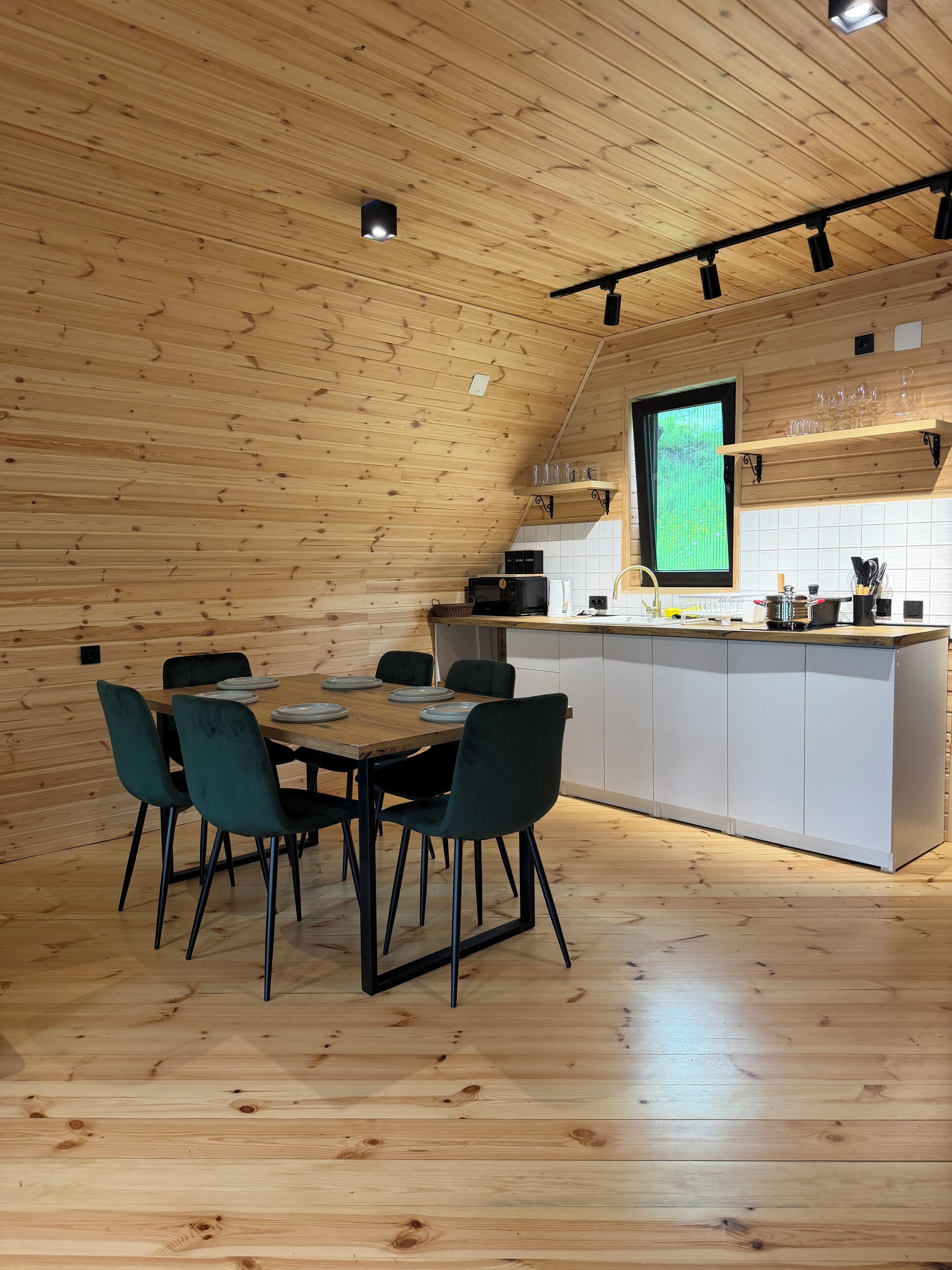 A wooden interior with a dining table, chairs, a kitchen area, and a window.