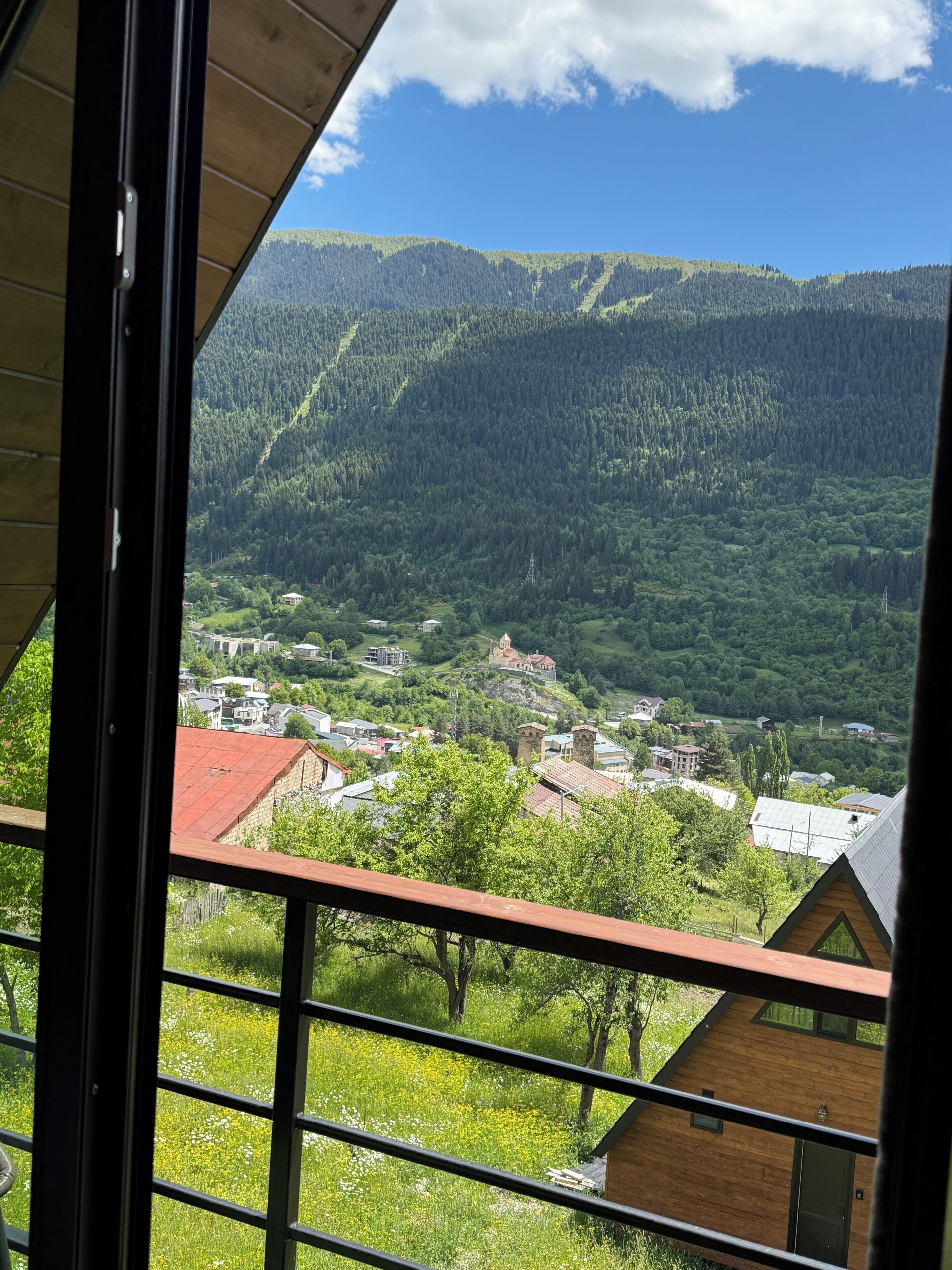 A view from a window overlooking a town with a mountain backdrop, a church, and a mix of residential and commercial buildings.