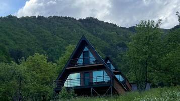 Un bâtiment moderne de forme triangulaire, doté de grandes fenêtres et entouré d’une végétation luxuriante et de montagnes.