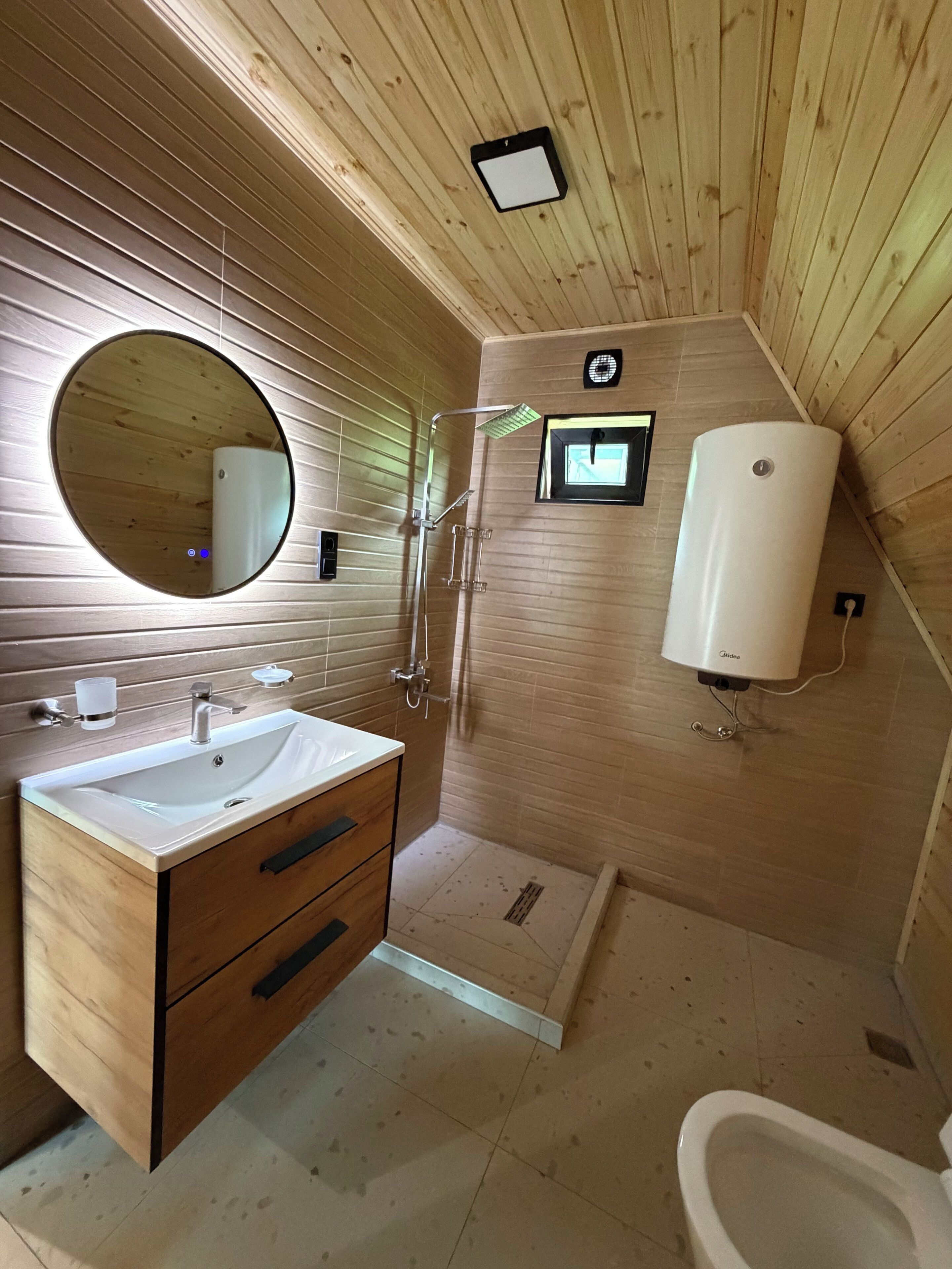 A wooden-paneled bathroom with a sink, mirror, shower, and toilet.