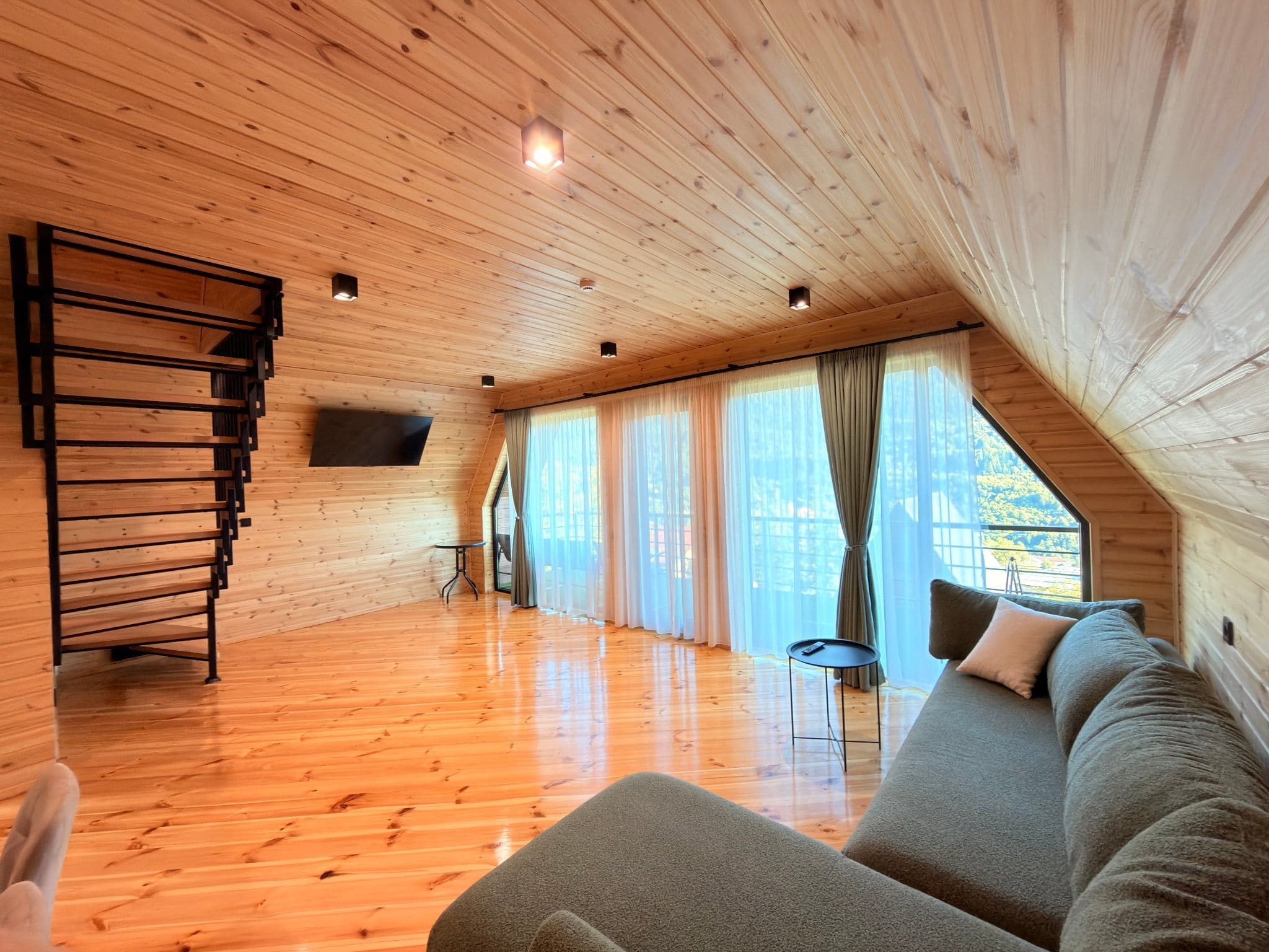 A wooden interior with a sofa, a TV, and a staircase.