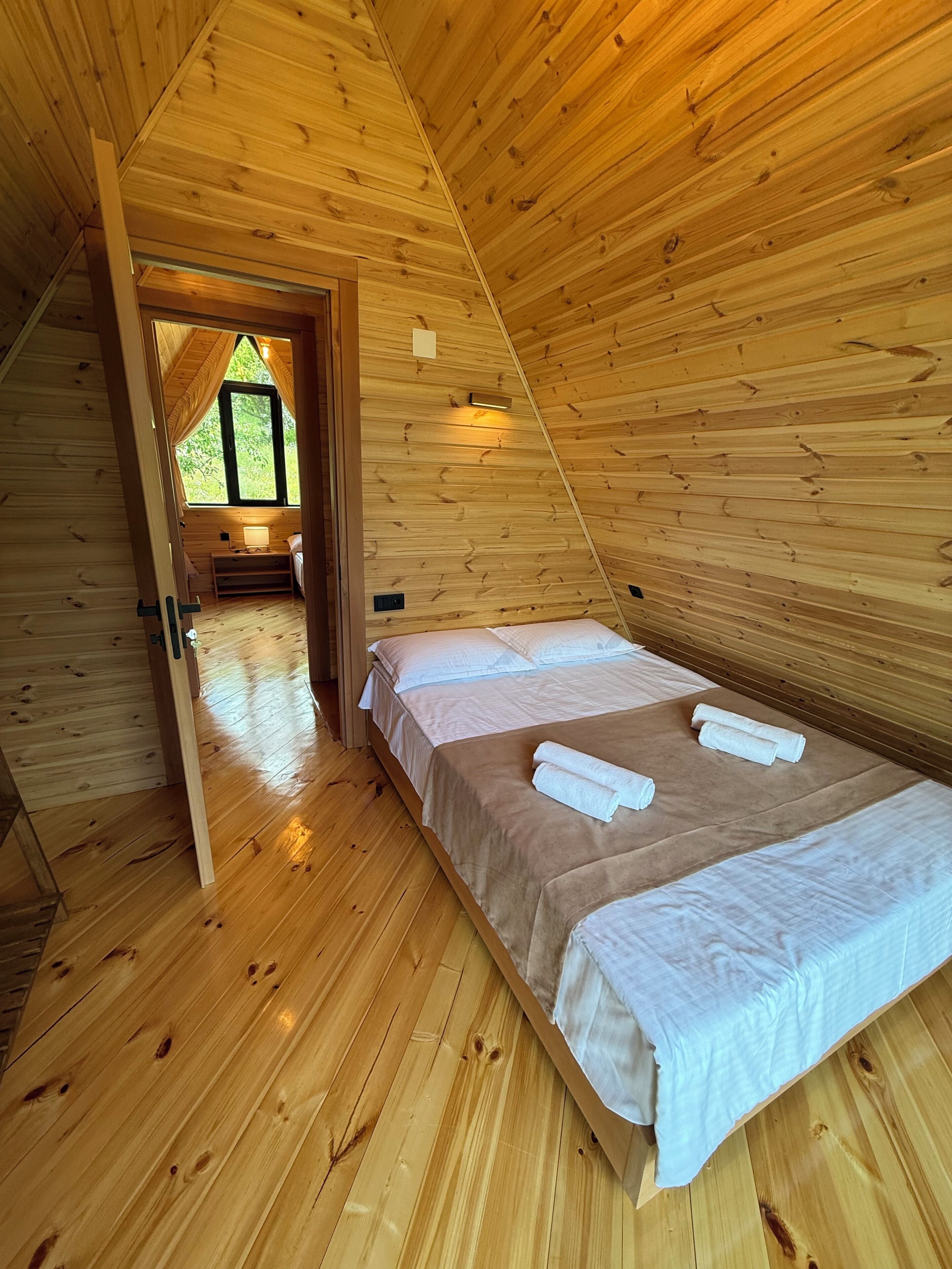 A wooden interior with a bed, a window, and a door leading to another room.