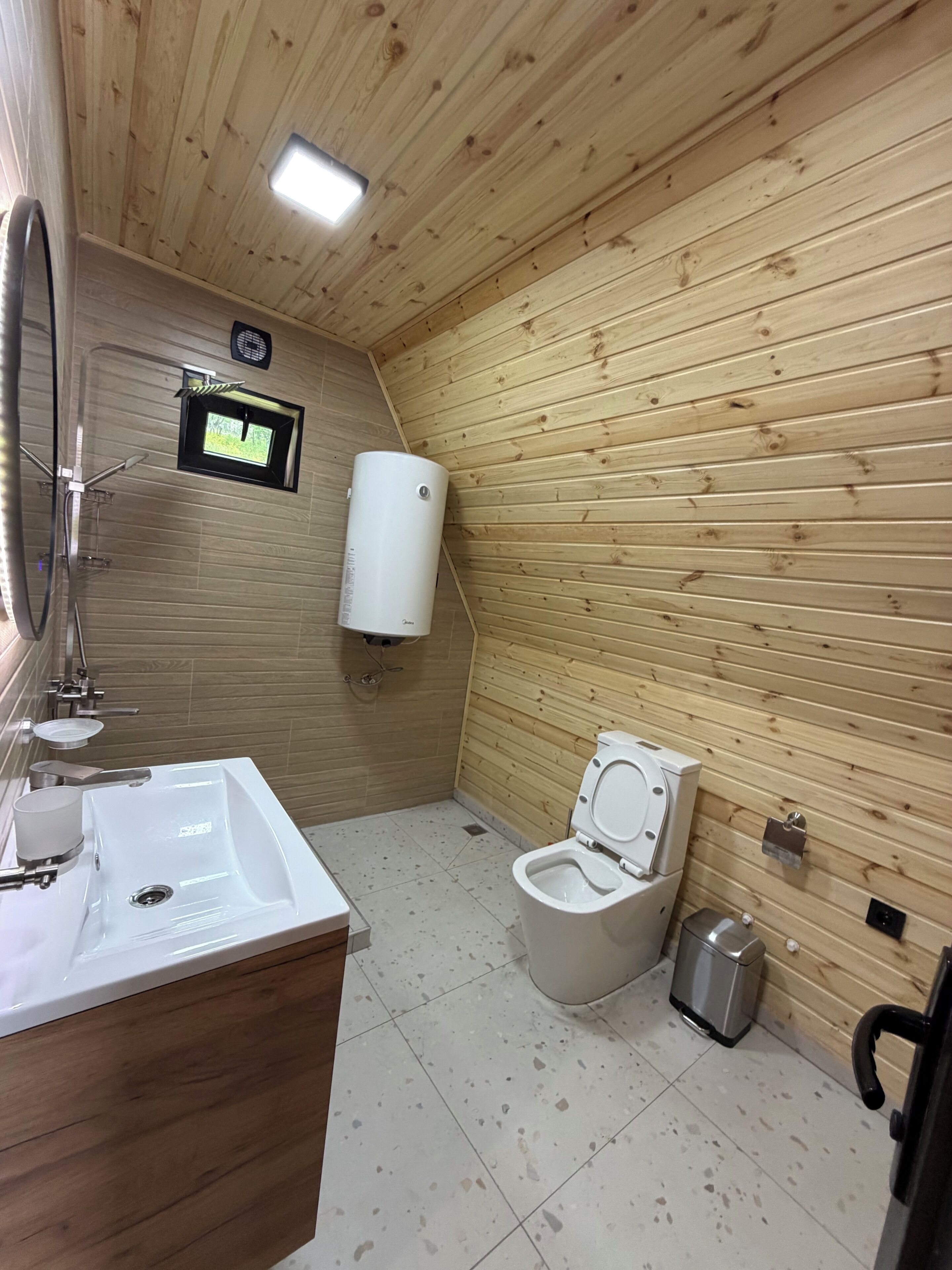 A wooden-paneled bathroom with a sink, toilet, and a small window.