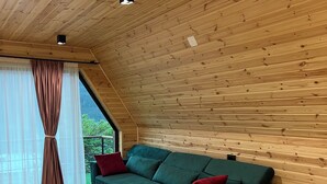 Una habitación acogedora con techo de madera, un sofá verde, una mesa de madera y un ventanal con cortinas ligeras.