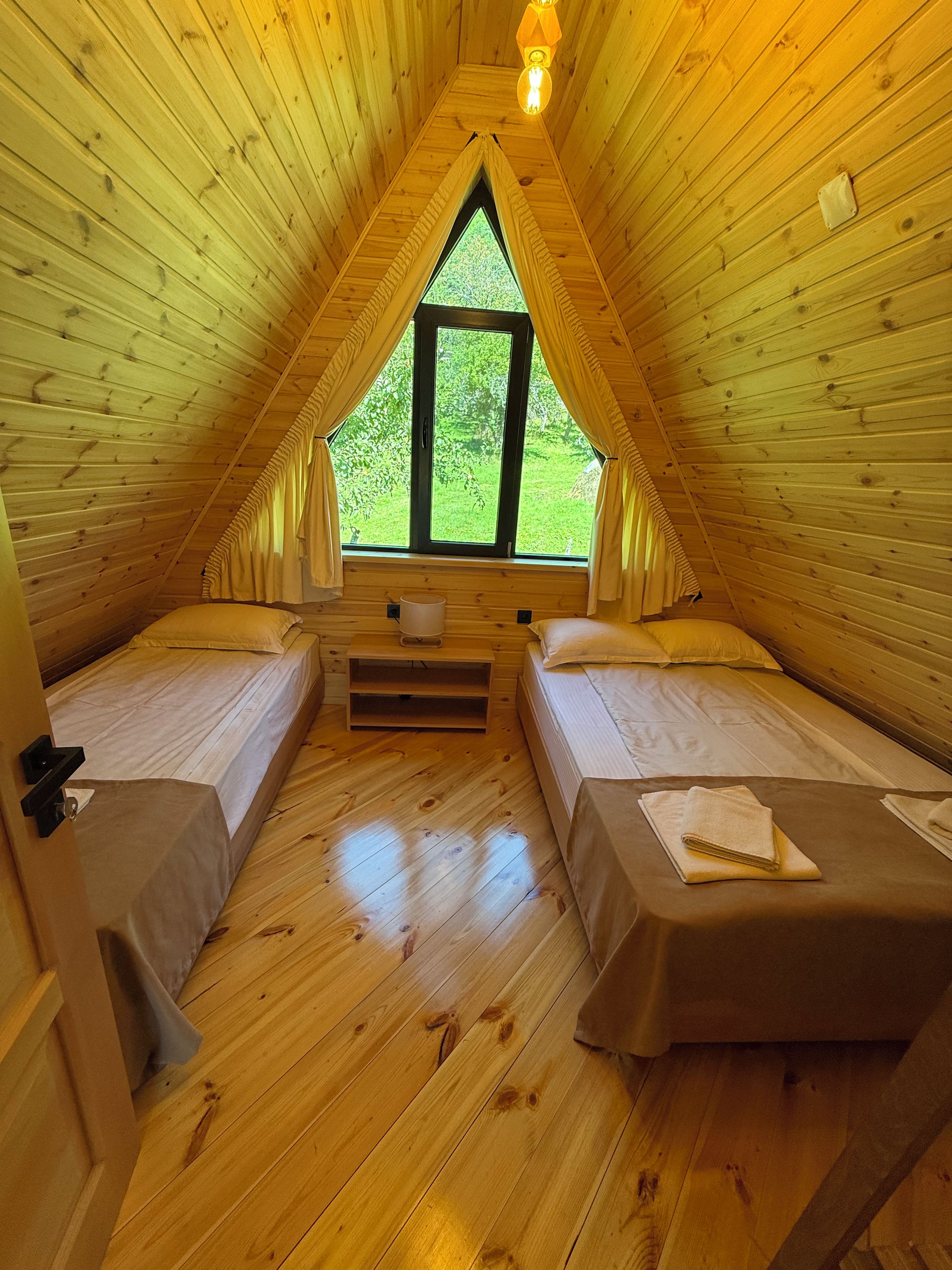 A cozy attic bedroom with two beds, a window, and a wooden ceiling.