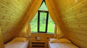 A cozy attic bedroom with two beds, a window, and a wooden ceiling.