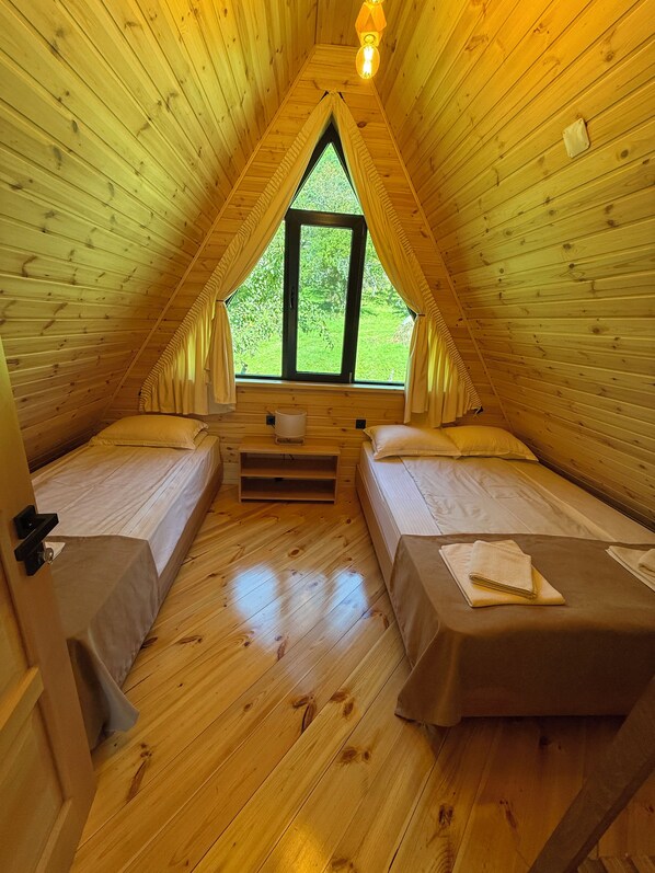A cozy attic bedroom with two beds, a window, and a wooden ceiling.