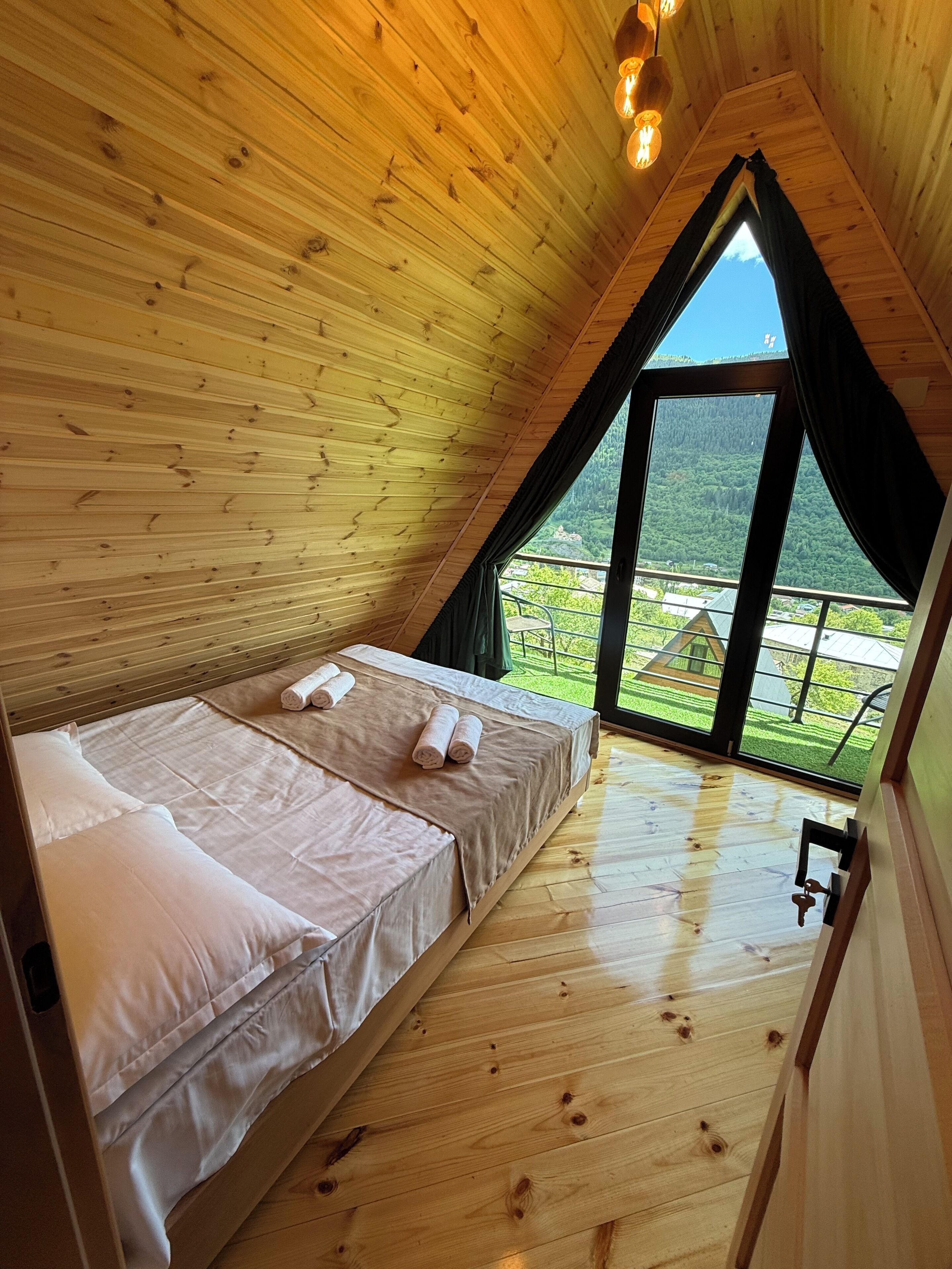 A wooden cabin with a loft-style bedroom, a large window, and a wooden floor.