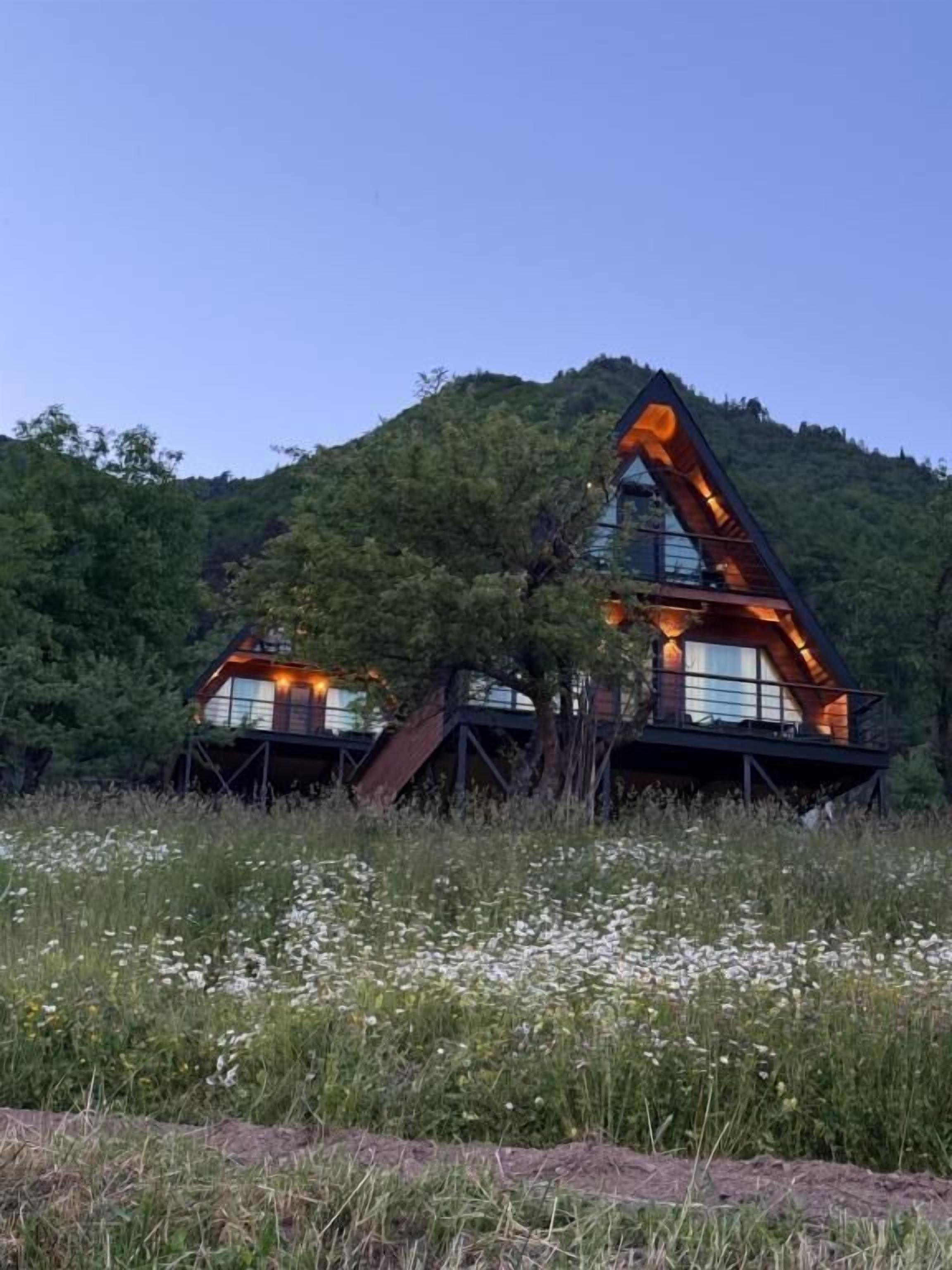 Een modern huis met een opvallende, driehoekige dakconstructie, omgeven door een natuurlijke omgeving.