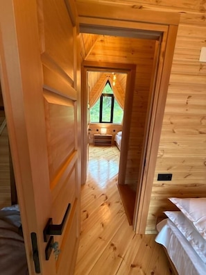 A wooden interior with a narrow hallway leading to a bedroom with a window.