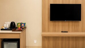 Quarto de hotel com televisão de ecrã plano na parede, comodidades para café com chaleira e snacks, e um mini frigorífico.
