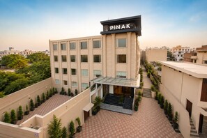 Un edificio de varios pisos con techo plano, un letrero que dice 'PINAK' y una entrada central con toldo de vidrio.