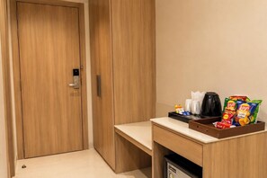 A hotel room with a wooden wardrobe, a small desk with a tray of snacks, a coffee maker, and a trash bin. - Hotel Pinak (Varanasi)
