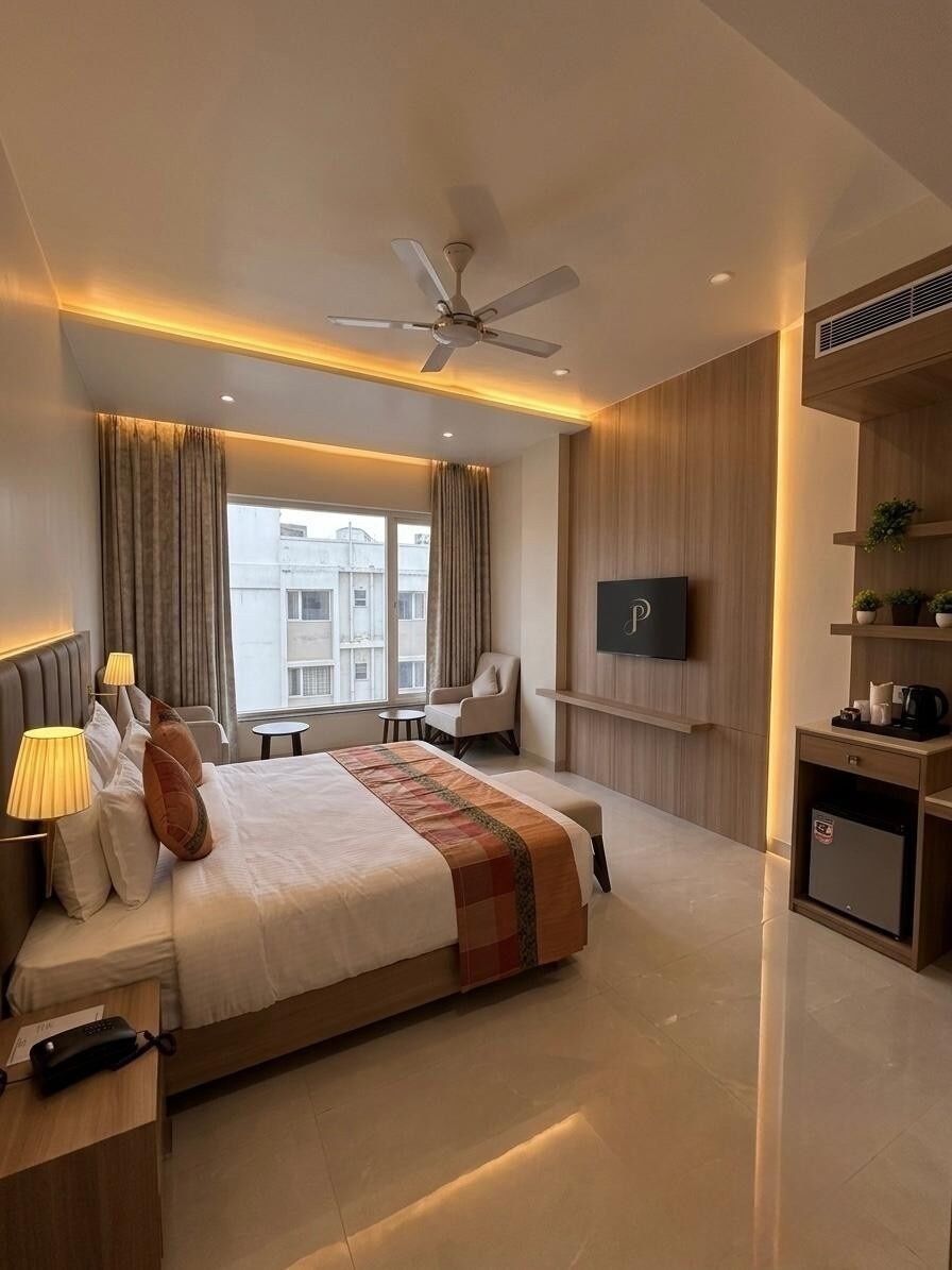 A modern hotel room with a bed, bedside tables, a desk, a chair, a TV, and a window with curtains.