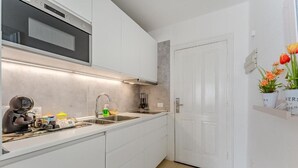 A modern kitchen with white cabinets, a built-in oven, a sink, and a countertop with various items. - Home Holidays 204 (CN)