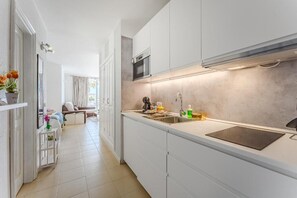 A modern kitchen with white cabinetry, a stainless steel sink, and a microwave. - Home Holidays 204 (CN)