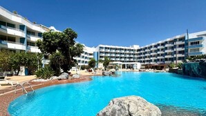 A hotel with a large swimming pool, multiple balconies, and a tropical landscape. - Home Holidays 204 (CN)