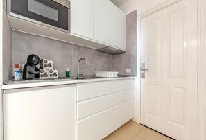 A kitchen with white cabinets, a stainless steel sink, and a microwave. - Home Holidays 204 (CN)