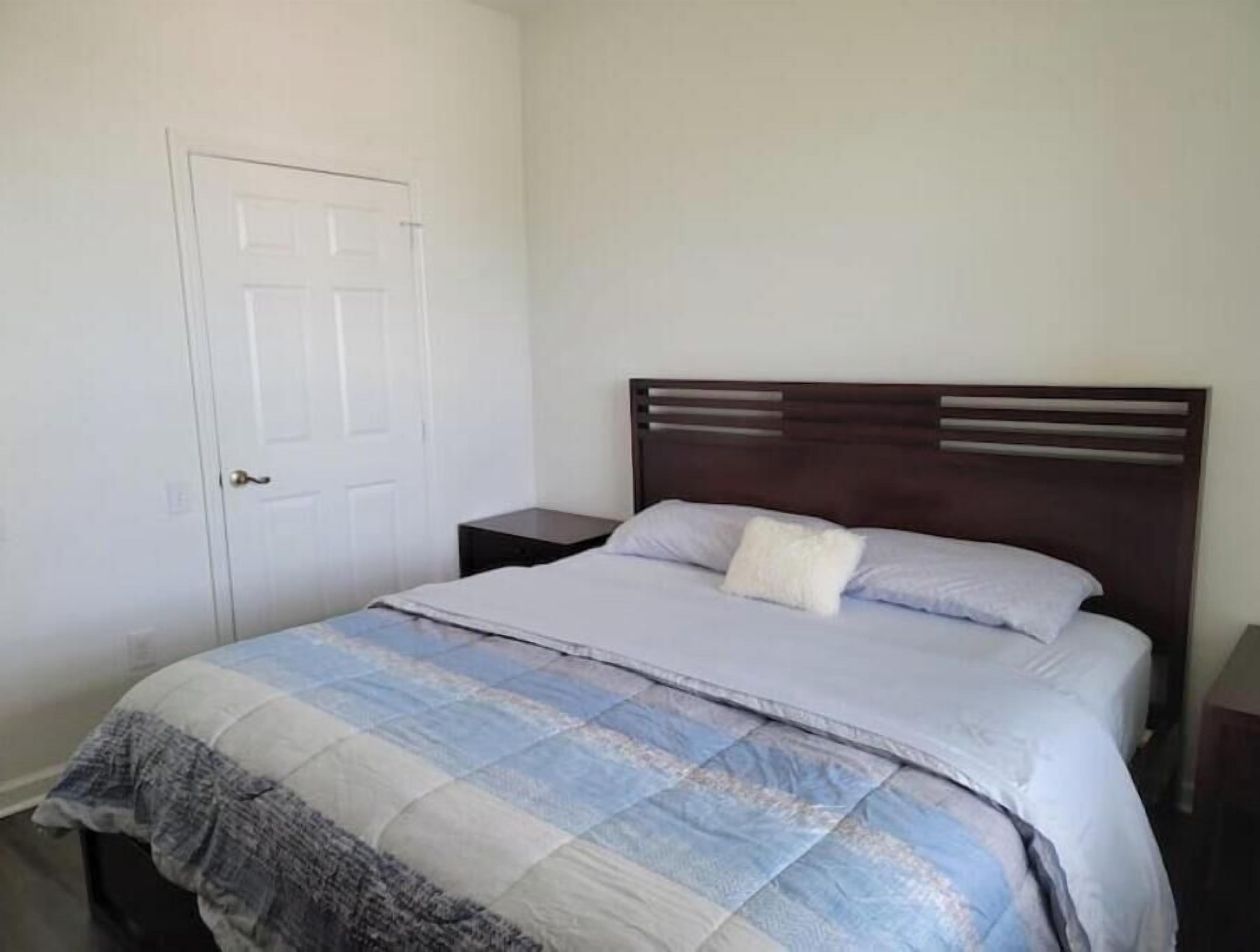 A bedroom with a bed, a nightstand, a door, and a wall.